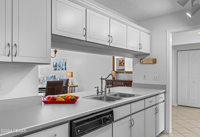 kitchen with light tile patterned flooring, white cabinetry, sink, dishwashing machine, and a textured ceiling