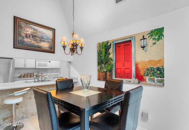 dining room with light wood-type flooring, a textured ceiling, a notable chandelier, sink, and vaulted ceiling