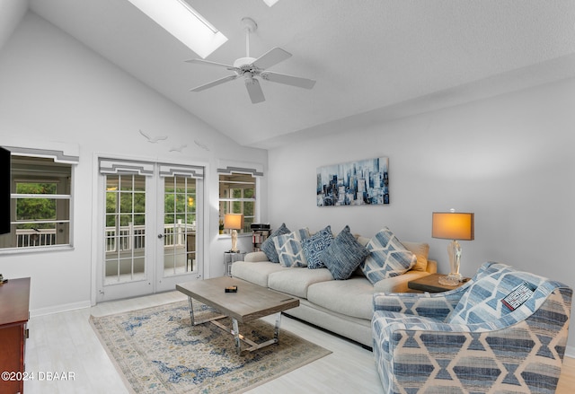 living room featuring french doors, high vaulted ceiling, a skylight, ceiling fan, and light hardwood / wood-style flooring