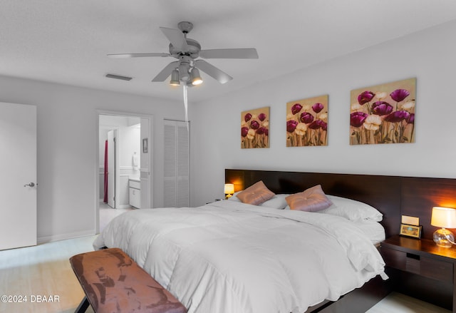 bedroom featuring light hardwood / wood-style floors, ensuite bath, ceiling fan, and a closet