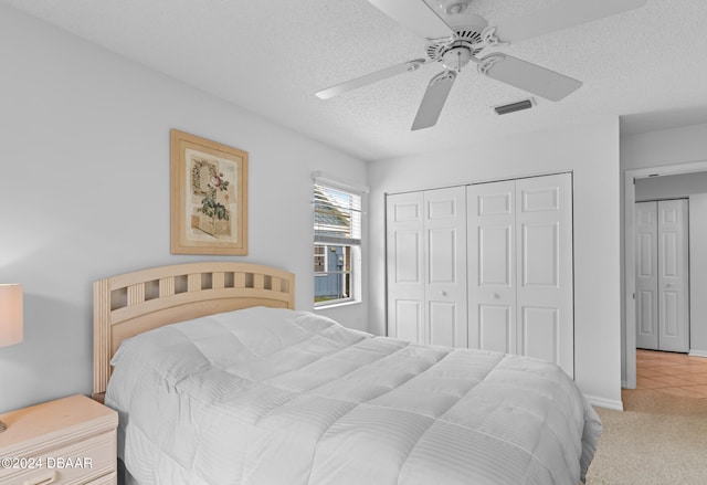 carpeted bedroom with a textured ceiling, ceiling fan, and a closet