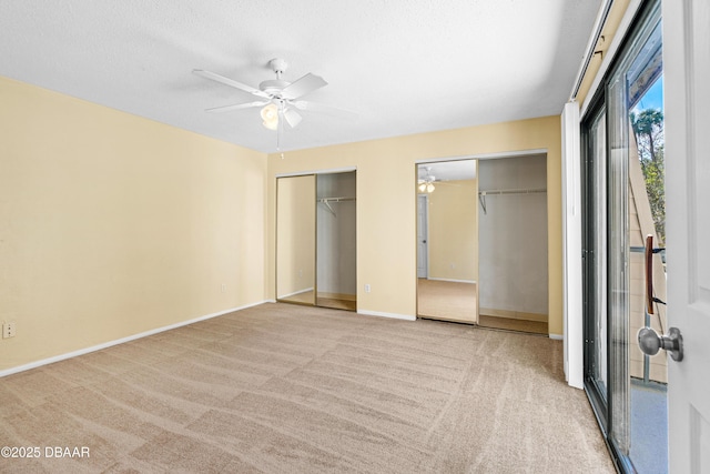 unfurnished bedroom with ceiling fan, multiple closets, light carpet, and a textured ceiling