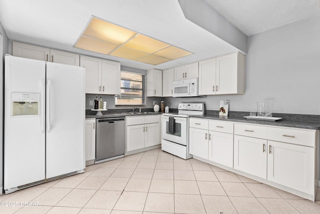 kitchen with light tile patterned floors, white cabinetry, sink, and white appliances