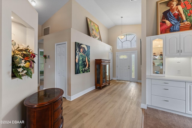 foyer entrance with high vaulted ceiling, light hardwood / wood-style floors, a notable chandelier, and a textured ceiling