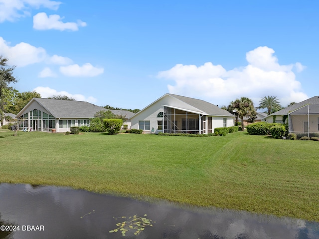 rear view of property with a sunroom, a yard, and a water view