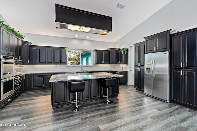 kitchen with a center island, lofted ceiling, backsplash, appliances with stainless steel finishes, and a kitchen bar