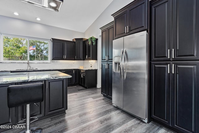 kitchen featuring light stone countertops, stainless steel refrigerator with ice dispenser, dark hardwood / wood-style flooring, backsplash, and vaulted ceiling