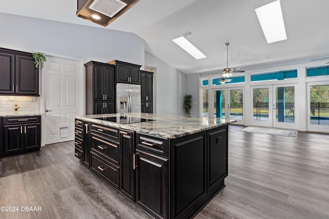 kitchen with french doors, stainless steel fridge with ice dispenser, lofted ceiling with skylight, black electric cooktop, and a kitchen island with sink