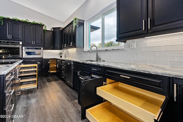 kitchen with backsplash, dark wood-type flooring, sink, vaulted ceiling, and light stone counters