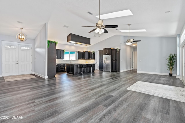 unfurnished living room featuring vaulted ceiling with skylight, dark wood-type flooring, ceiling fan with notable chandelier, and sink