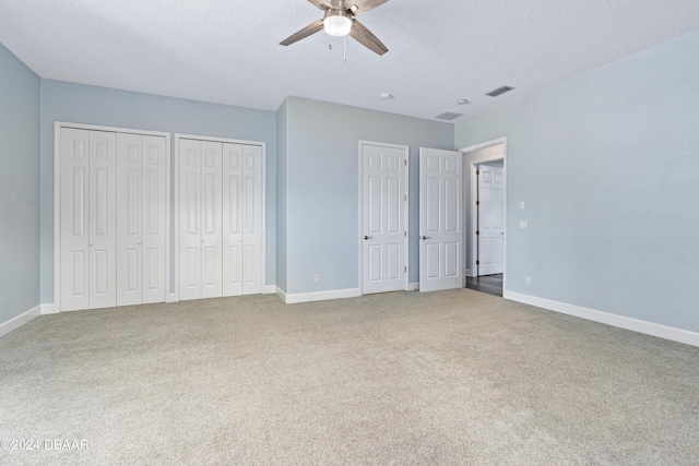 unfurnished bedroom featuring carpet flooring, multiple closets, ceiling fan, and a textured ceiling