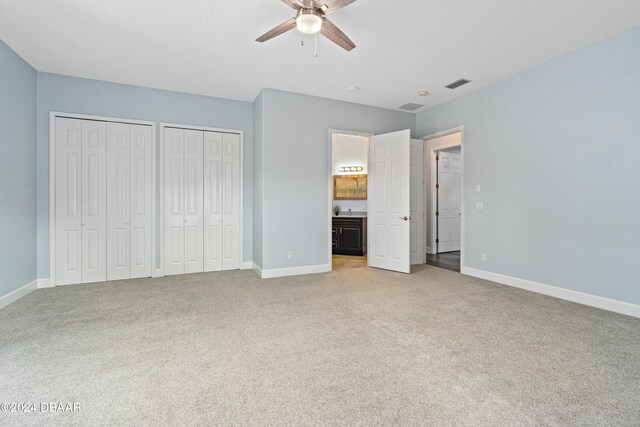 unfurnished bedroom with ensuite bath, ceiling fan, carpet floors, and two closets