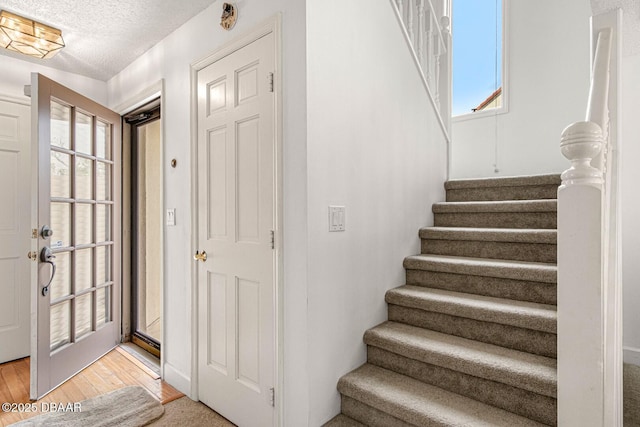 foyer entrance with stairs, light wood-style flooring, and a textured ceiling