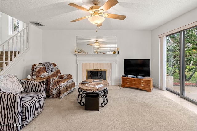 carpeted living room with plenty of natural light, a textured ceiling, stairs, and a tile fireplace