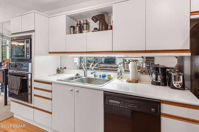 kitchen with white cabinets, black appliances, light countertops, and a sink