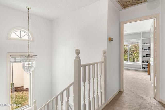 corridor with visible vents, carpet floors, an upstairs landing, a notable chandelier, and a textured ceiling