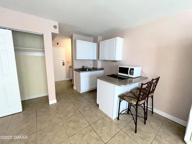 kitchen featuring a kitchen breakfast bar, dark countertops, a peninsula, white cabinets, and white microwave