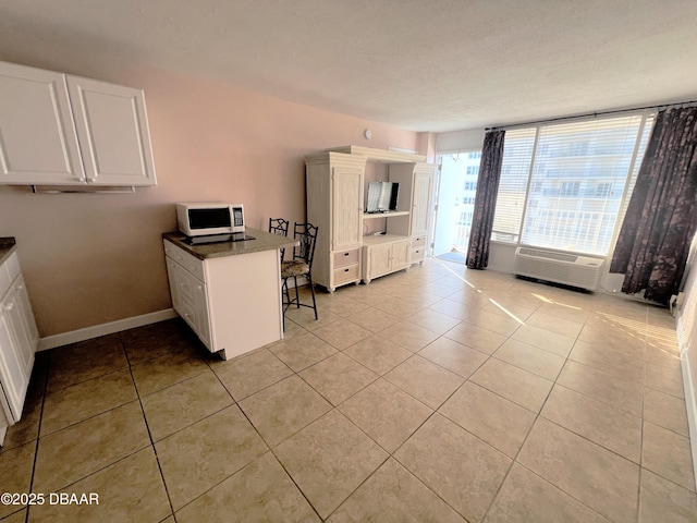 kitchen with light tile patterned floors, white microwave, a peninsula, and white cabinets