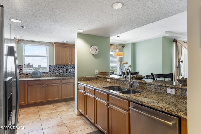 kitchen featuring appliances with stainless steel finishes, a sink, brown cabinets, a textured ceiling, and pendant lighting