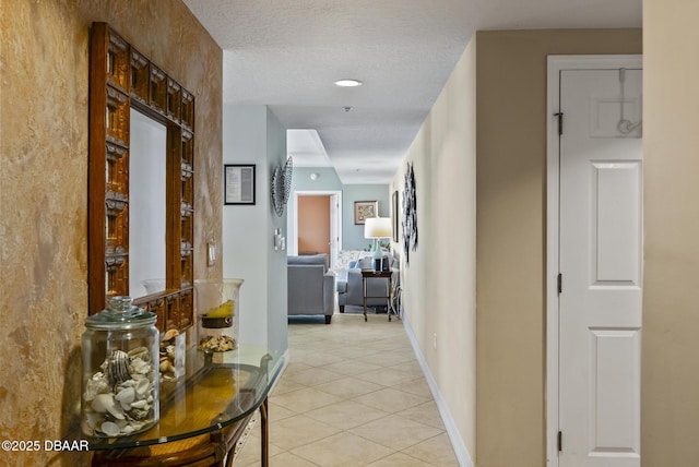 hall featuring light tile patterned floors, a textured ceiling, and baseboards