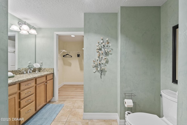 bathroom featuring toilet, tile patterned floors, vanity, a textured ceiling, and a spacious closet