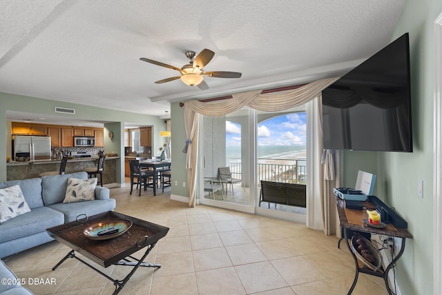 living area featuring ceiling fan, light tile patterned floors, a textured ceiling, and baseboards