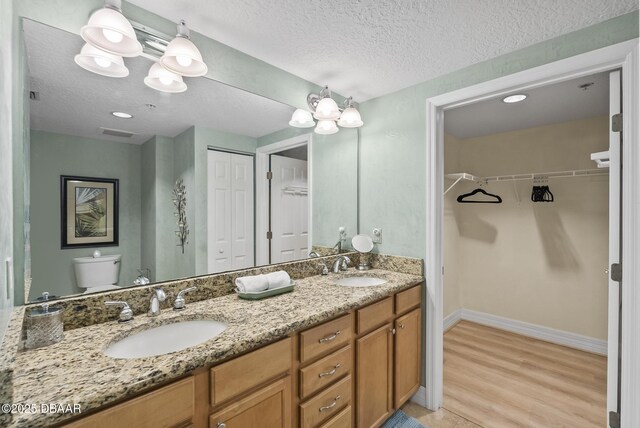 bathroom with a textured ceiling, toilet, baseboards, double vanity, and wood finished floors