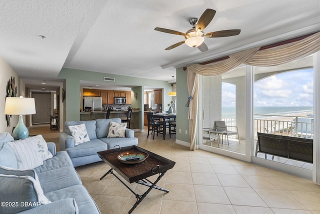 living room with a water view, ceiling fan, light tile patterned flooring, a textured ceiling, and baseboards