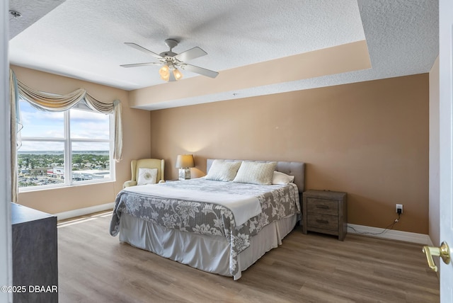 bedroom with a textured ceiling, wood finished floors, baseboards, and ceiling fan