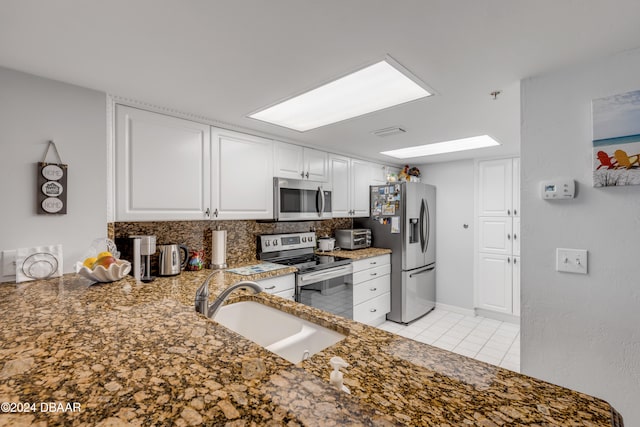 kitchen with kitchen peninsula, sink, light tile patterned floors, white cabinetry, and appliances with stainless steel finishes