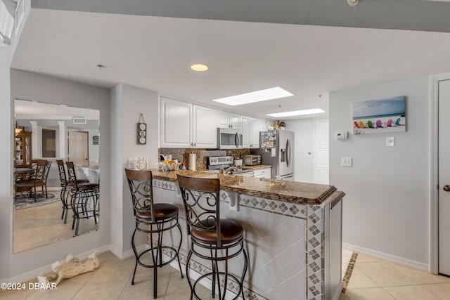 kitchen with light tile patterned flooring, appliances with stainless steel finishes, white cabinets, a breakfast bar area, and kitchen peninsula