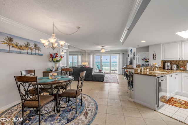 tiled dining space with sink, a textured ceiling, ornamental molding, and ceiling fan with notable chandelier