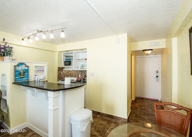 kitchen with built in microwave, a textured ceiling, dark tile patterned floors, and backsplash