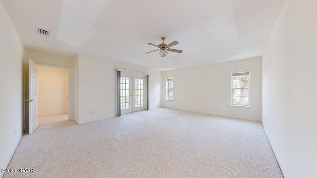 unfurnished room with visible vents, light carpet, a ceiling fan, a tray ceiling, and french doors