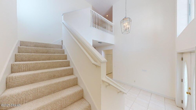 stairway with tile patterned floors, a high ceiling, a notable chandelier, and baseboards