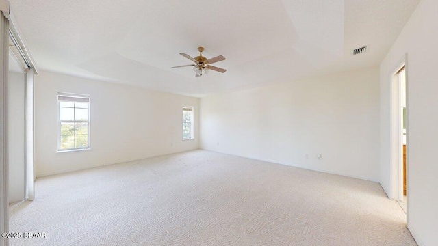 spare room featuring a tray ceiling, light colored carpet, visible vents, and a ceiling fan