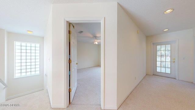 corridor with recessed lighting, light colored carpet, a wealth of natural light, and a textured ceiling