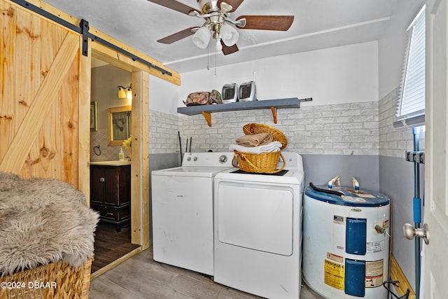 clothes washing area featuring water heater, a barn door, ceiling fan, light hardwood / wood-style flooring, and independent washer and dryer