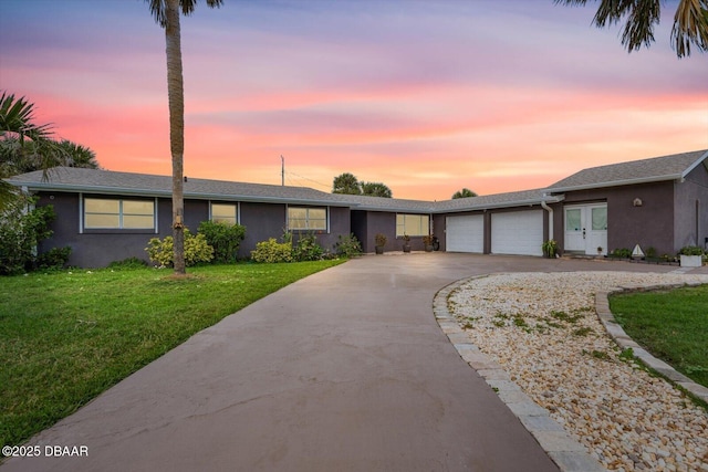 ranch-style house featuring an attached garage, concrete driveway, french doors, a lawn, and stucco siding