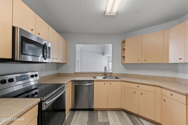 kitchen with light brown cabinets, sink, a textured ceiling, light hardwood / wood-style floors, and stainless steel appliances