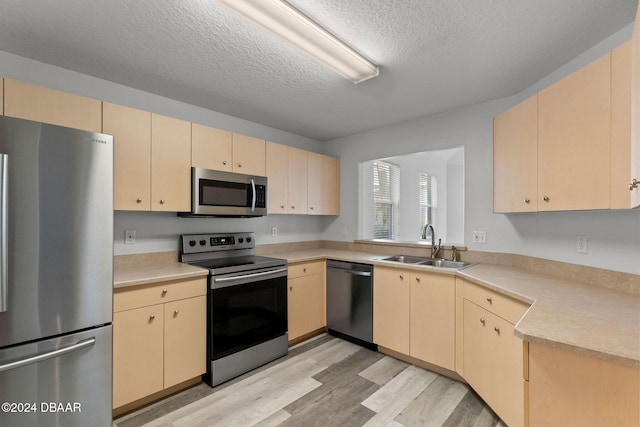 kitchen featuring sink, light hardwood / wood-style flooring, a textured ceiling, light brown cabinetry, and stainless steel appliances