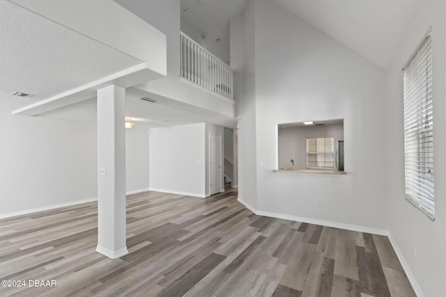 unfurnished living room featuring hardwood / wood-style floors, high vaulted ceiling, and a textured ceiling