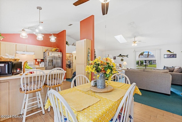 dining space with ceiling fan, light hardwood / wood-style floors, and lofted ceiling with skylight