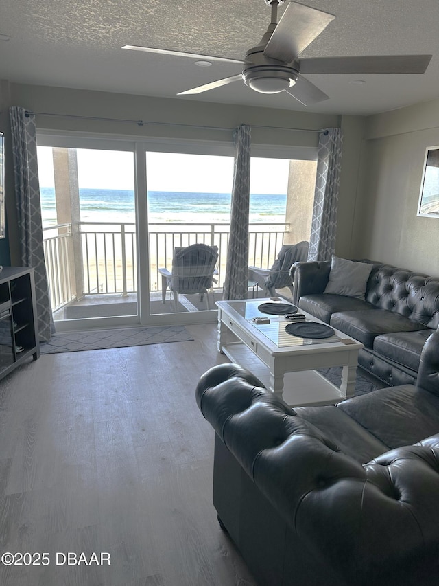 living room featuring a beach view, a water view, wood-type flooring, a textured ceiling, and ceiling fan