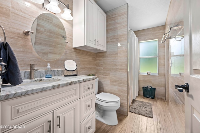 bathroom with wood-type flooring, vanity, toilet, and tile walls