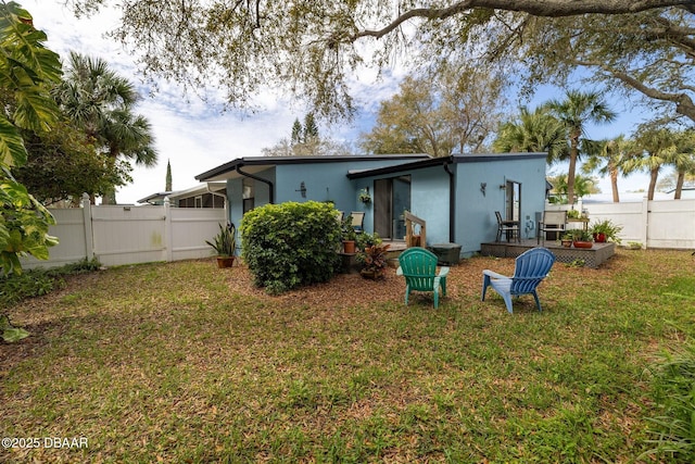 rear view of house featuring a yard, fence, and stucco siding