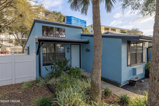 view of front of property featuring metal roof, fence, and stucco siding