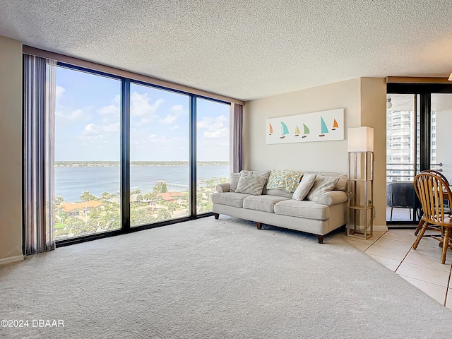 living area with a wall of windows, light colored carpet, a water view, and a textured ceiling