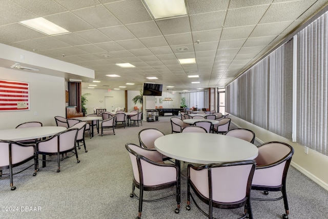 carpeted dining space featuring a drop ceiling and baseboards