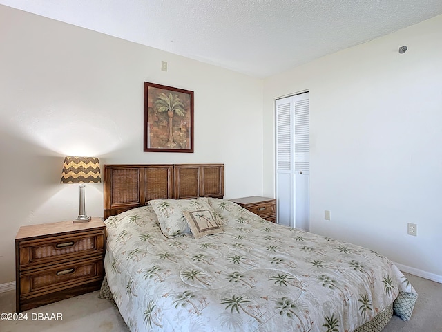 bedroom featuring a closet, light carpet, a textured ceiling, and baseboards